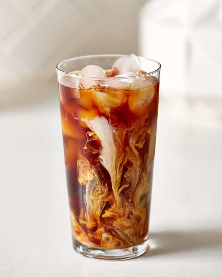 Iced coffee in a tall glass with swirling cream and ice cubes.