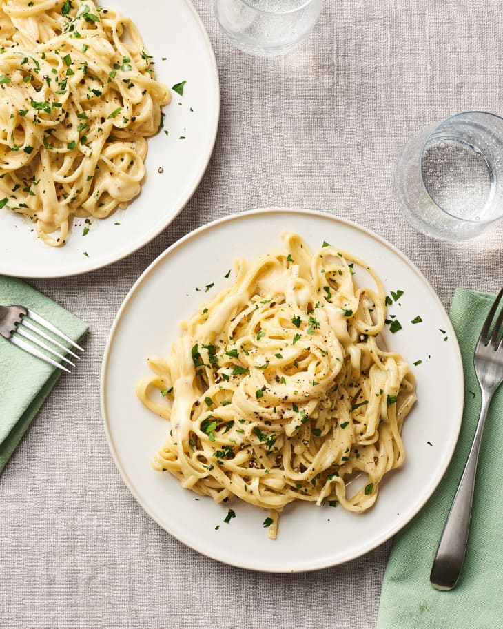 Overhead shot of two plates with servings of pasta in Alfredo sauce