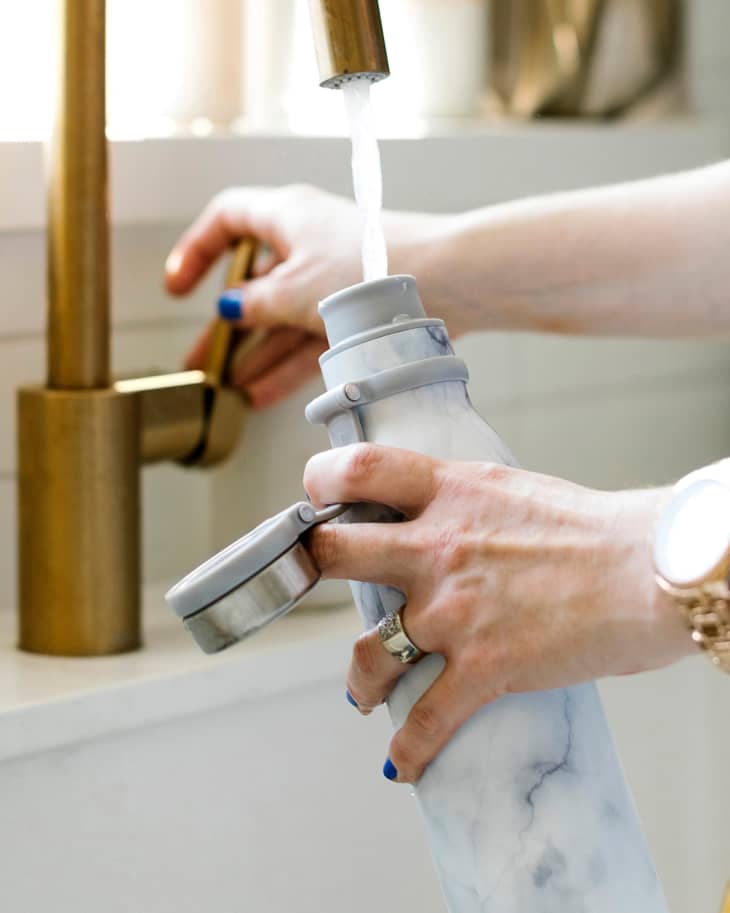 Hands of woman filling water bottle in kitchen sink