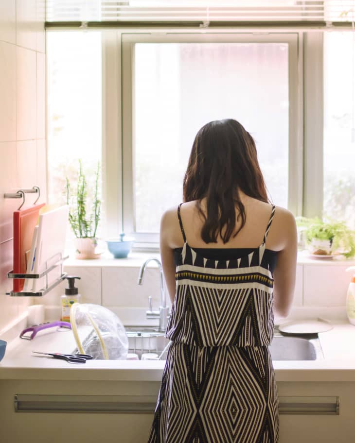 Rear view of woman at kitchen sink in front of window doing dishes