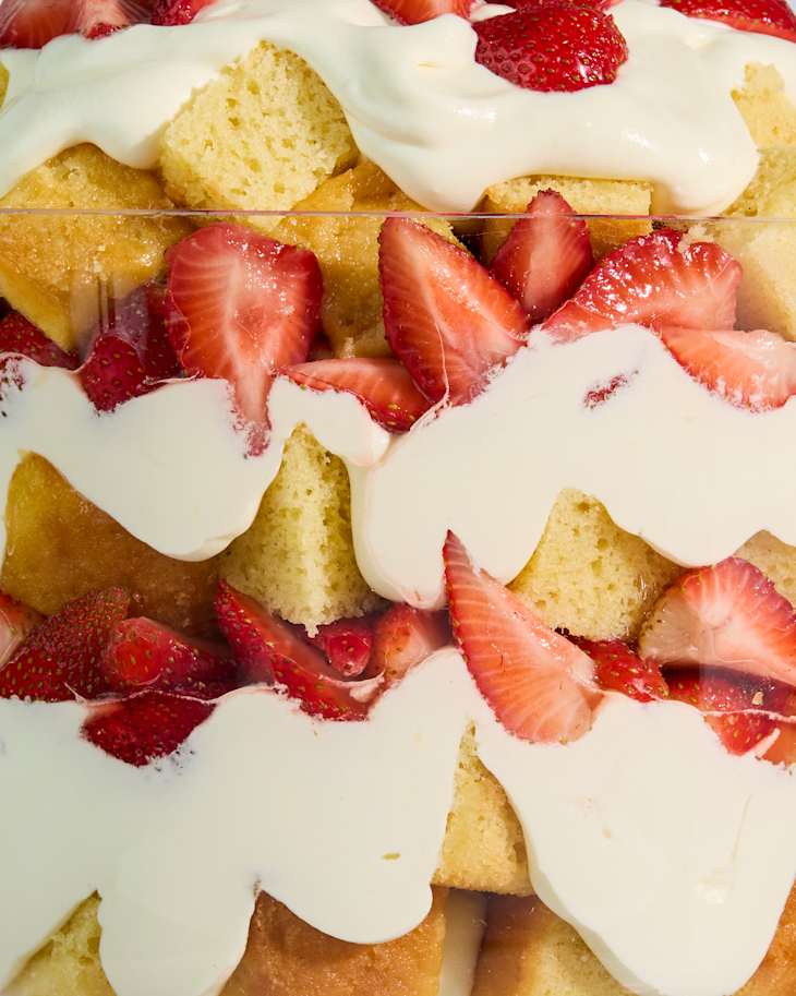 Layered dessert in a clear bowl with sponge cake, whipped cream, and fresh strawberries on top.