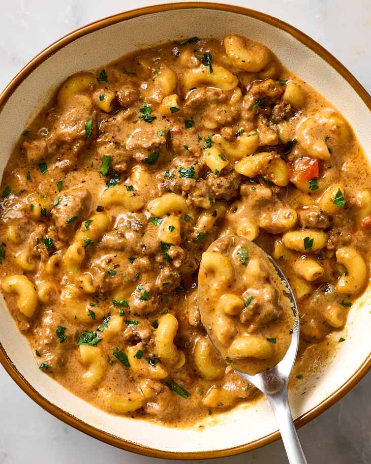 Creamy beef and macaroni dish in a bowl, garnished with parsley and served with a spoon.