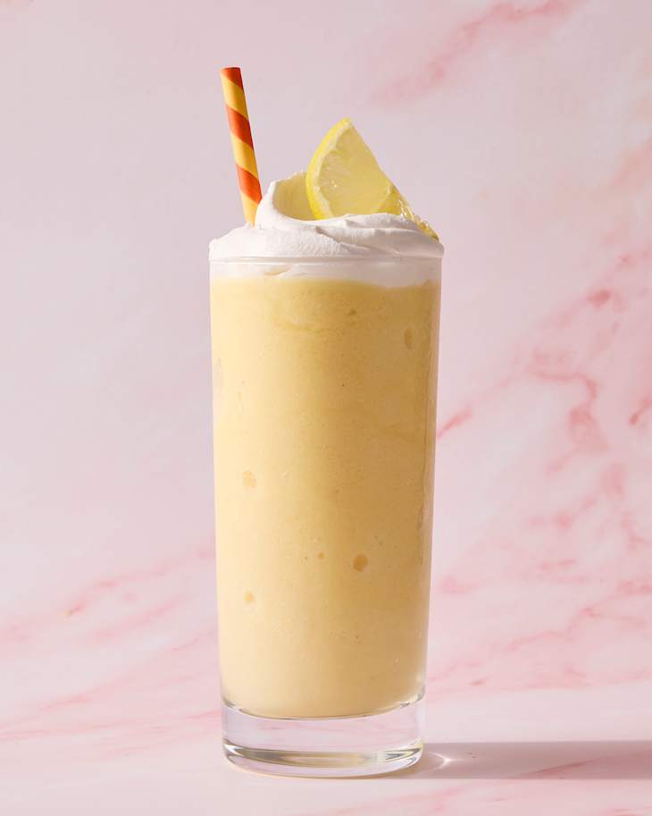 Frosted lemon drink topped with whipped cream and a lemon slice, served with a striped straw.