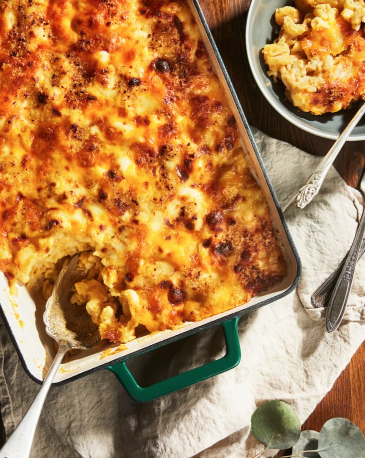 Baked macaroni and cheese in a casserole dish with a serving spoon, next to a plate with a portion served.