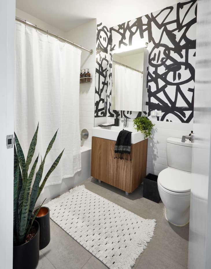 Modern bathroom with abstract black and white wall, wooden vanity, white shower curtain, and potted snake plant.