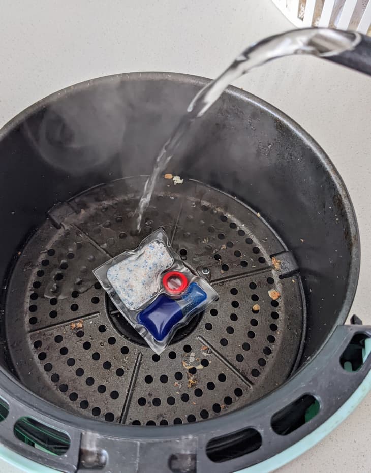 Water being poured over a detergent pod in an air fryer basket.