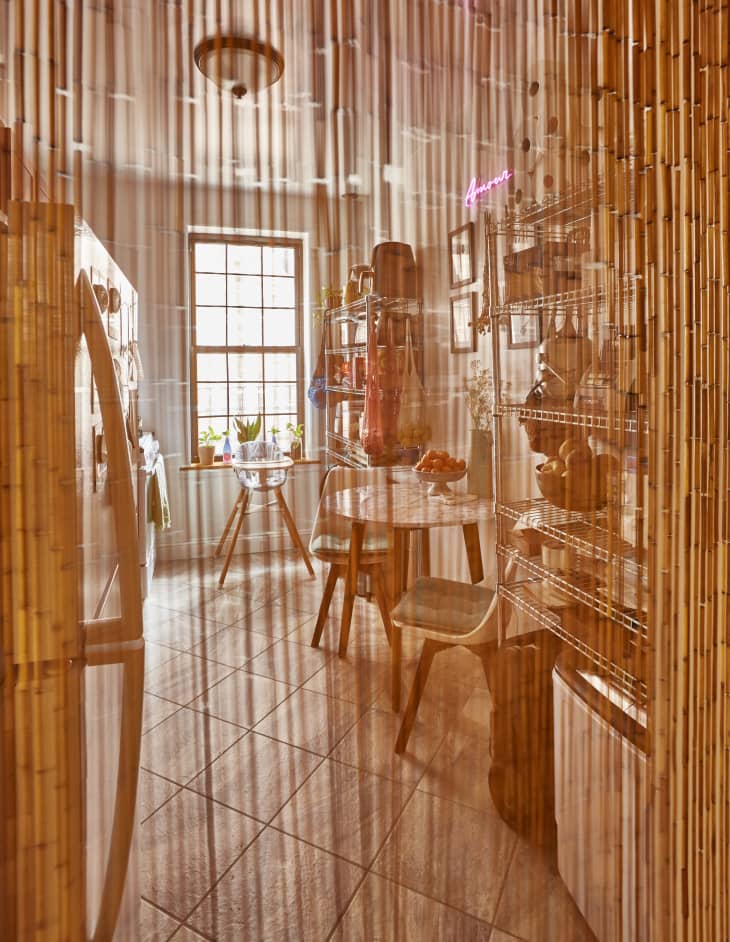Cozy kitchen with bamboo curtain, round table, chairs, metal shelves, and a window with potted plants.