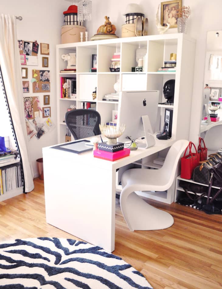 Home office with white desk, computer, black chair, white shelving, decor items, and a zebra-patterned rug.