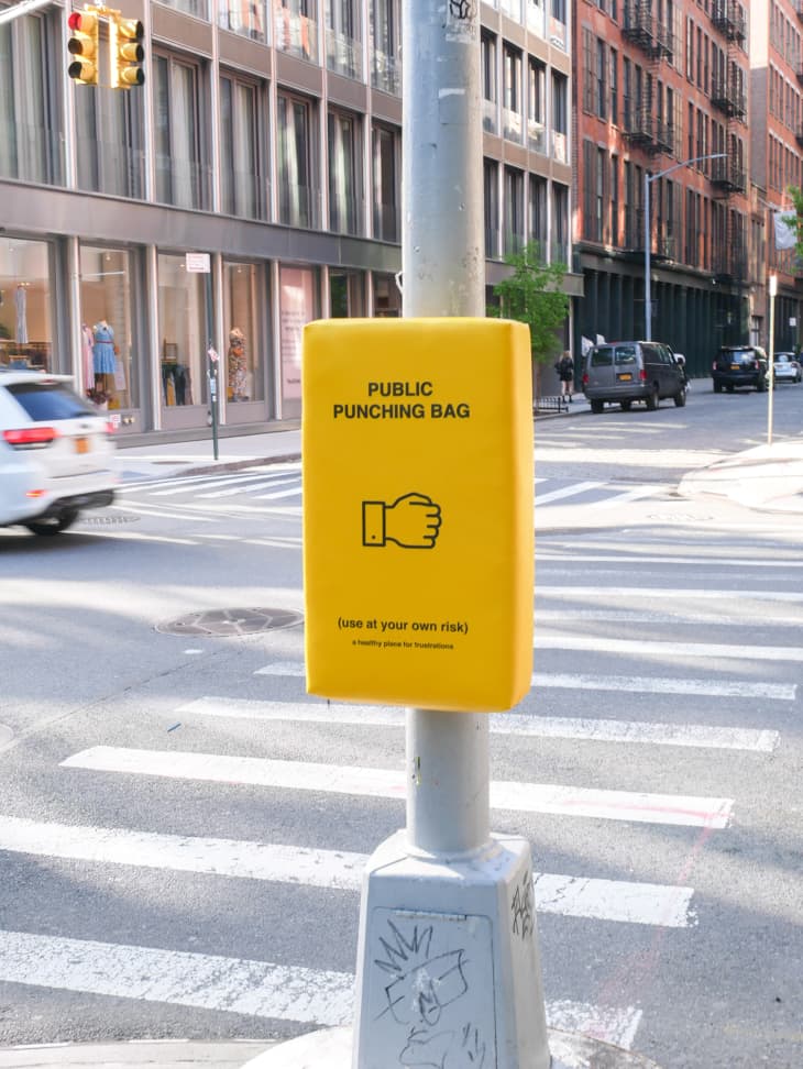 Yellow public punching bag on a street pole in an urban setting with buildings and traffic.