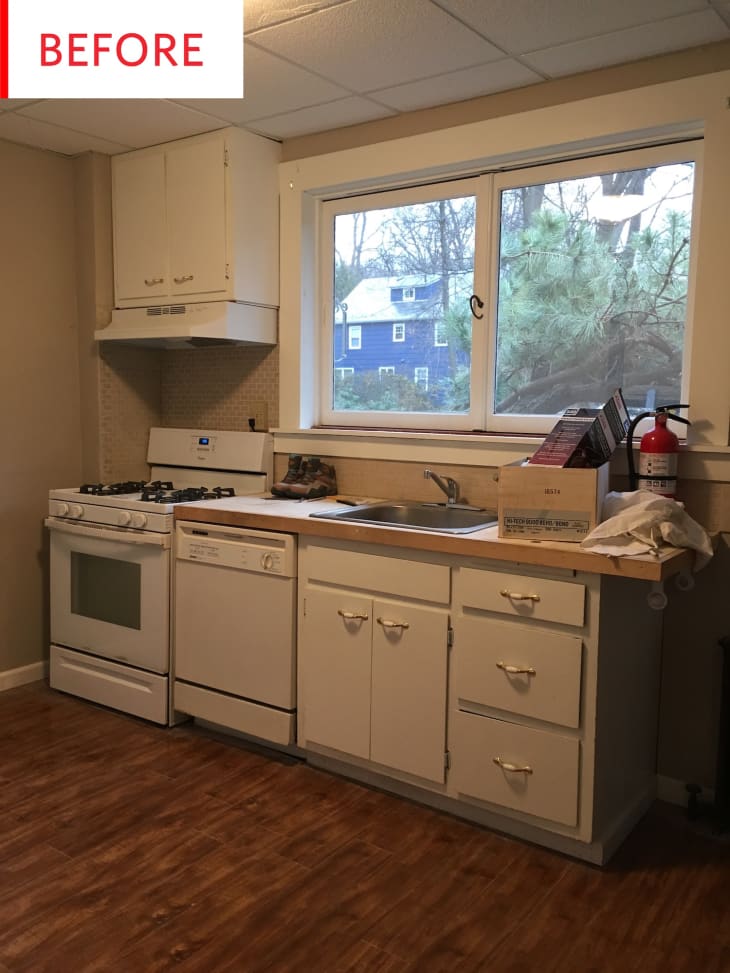 Small kitchen with white cabinets, gas stove, dishwasher, and large window overlooking trees.