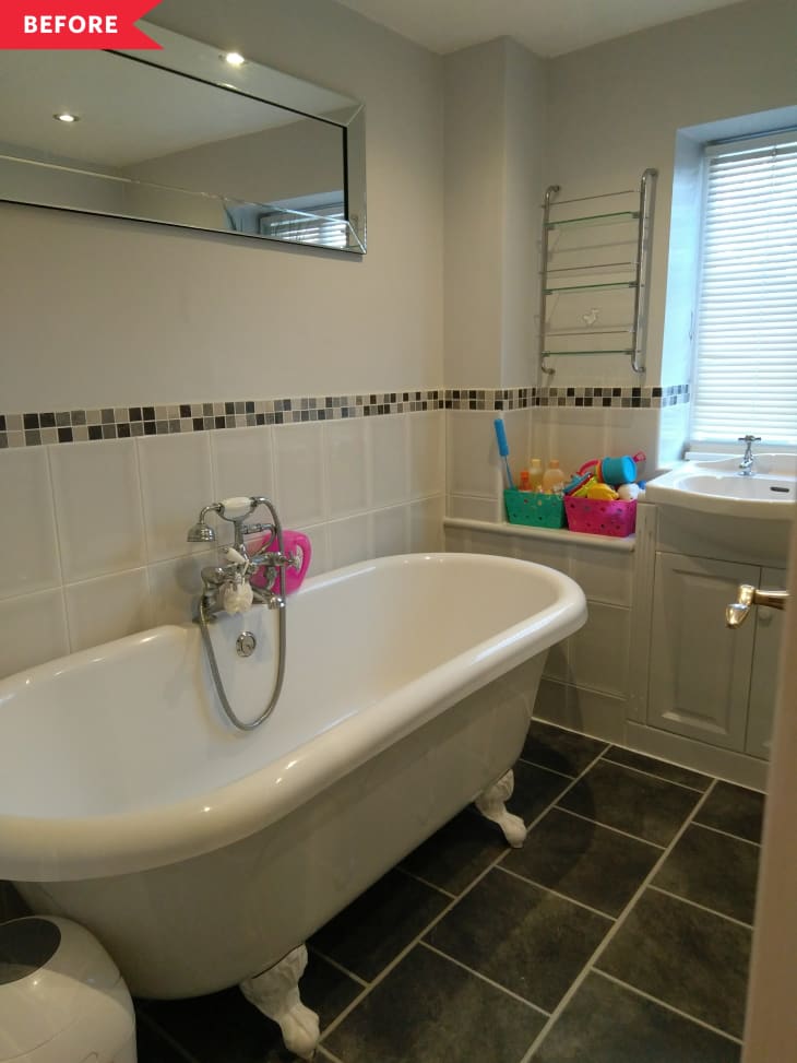 Clawfoot bathtub in a tiled bathroom with a mirror, towel rack, and colorful bath toys by the window.