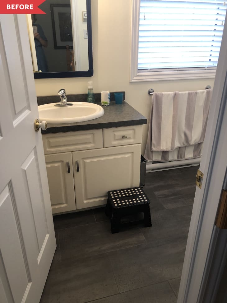 Small bathroom with white cabinets, gray countertop, sink, mirror, striped towel, and black step stool.