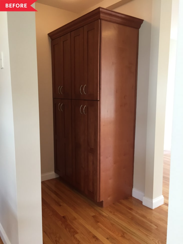Tall wooden cabinet with six doors in a narrow hallway, hardwood floor.