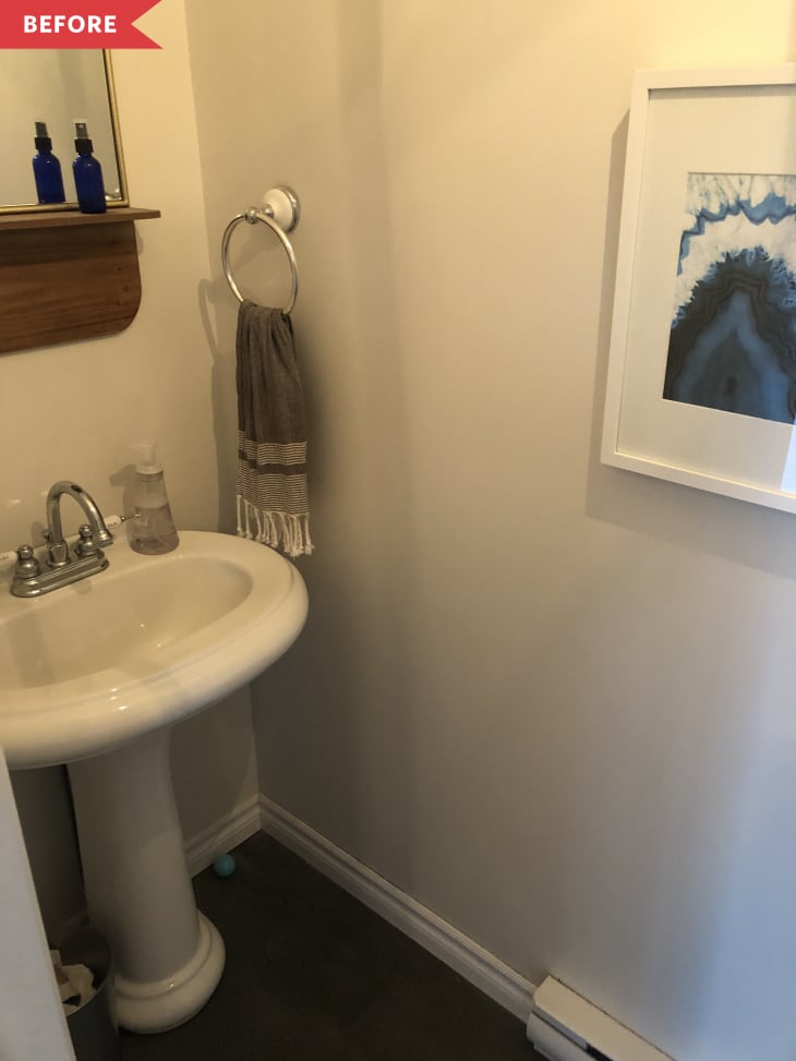 Small bathroom with pedestal sink, towel ring, blue bottles on a shelf, and framed abstract art.