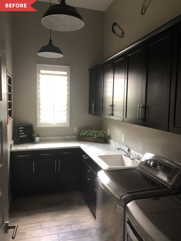 Laundry room with dark cabinets, marble countertop, washer, dryer, and a small plant under a window with shutters.