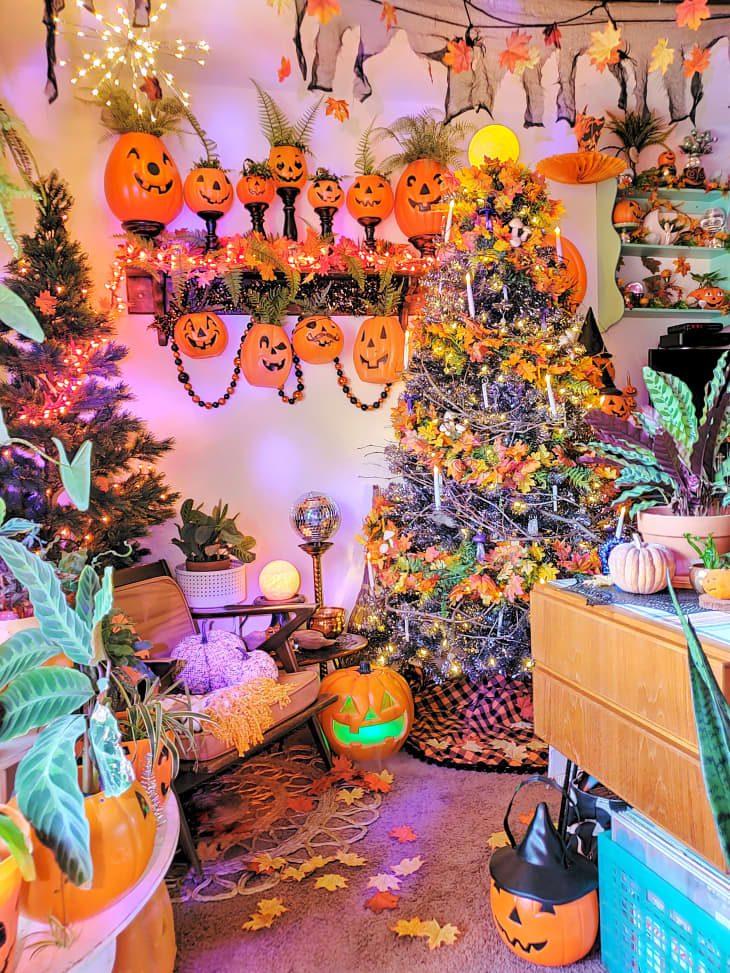 Image 2: Room decorated for Halloween with jack-o'-lanterns, a lit tree, autumn leaves, and festive lights.