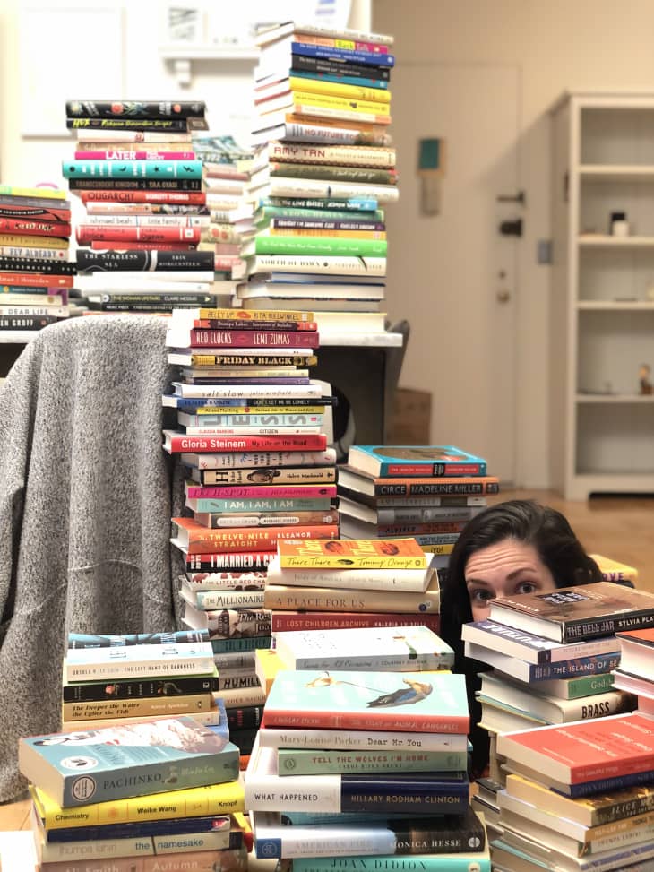 Stacks of colorful books piled high in a room, with a person peeking through the stacks.