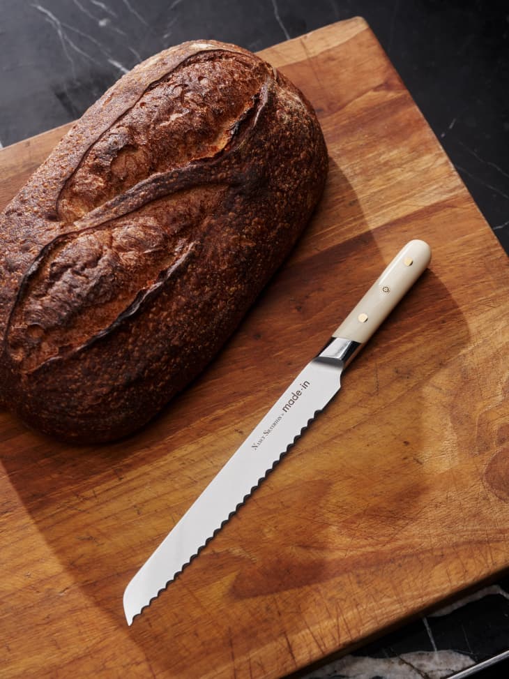 Sourdough loaf and serrated knife on a wooden cutting board.