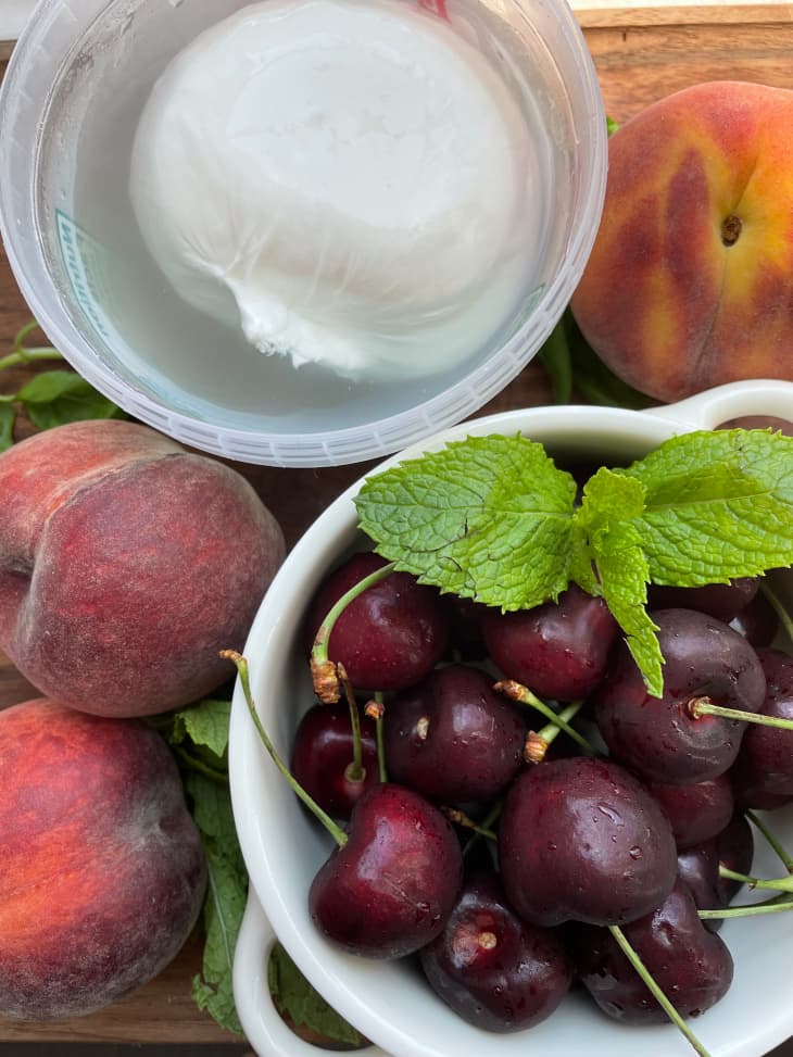 Ingredients for peach, cherry, burrata salad on wooden cutting board.