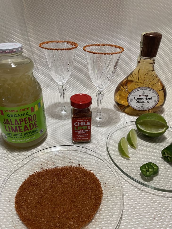 tajin on a plate, orange rim glasses, margarita mix, tequila, lime wedges on glass plate, jalapeno slices on glass plate
