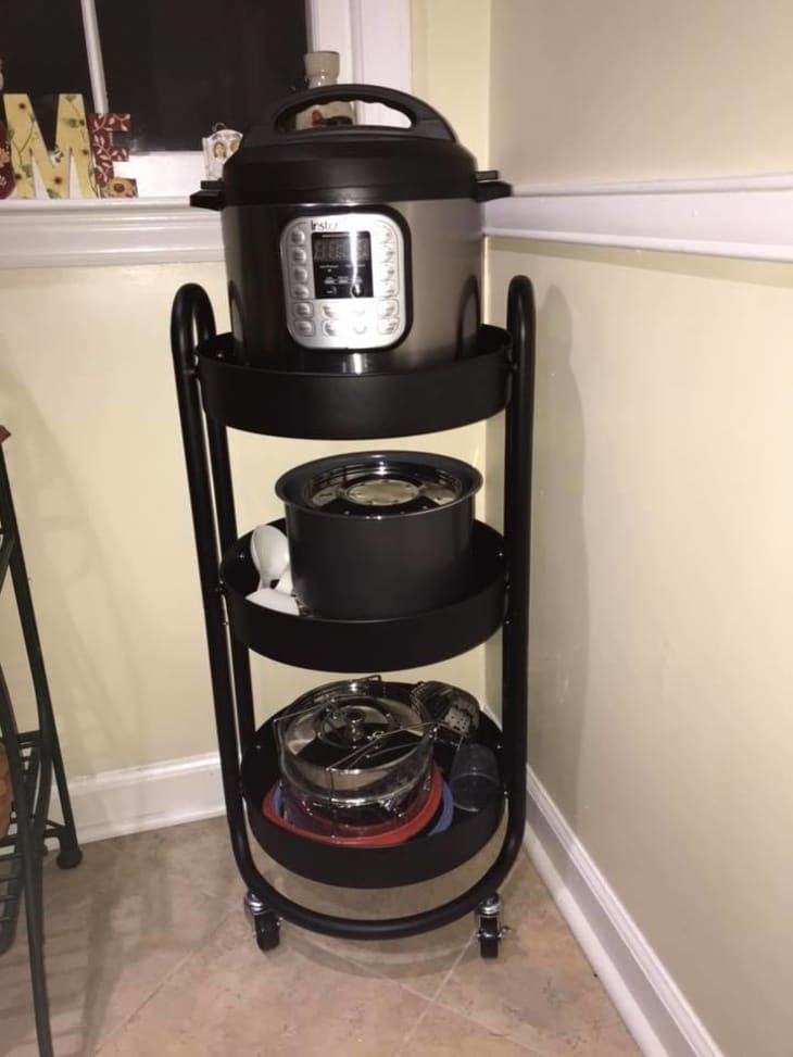 Three-tier black kitchen cart with an Instant Pot on top, cookware in the middle, and kitchen utensils on the bottom shelf.