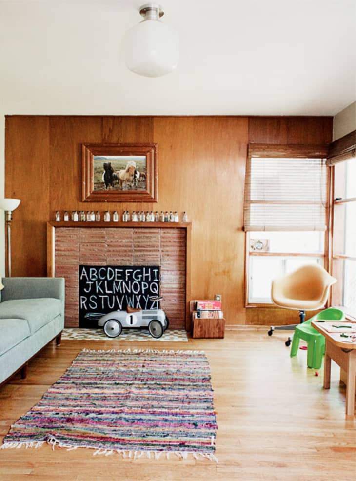 Living room with wood paneling, a blue sofa, colorful rug, toy car, and alphabet board by the fireplace.
