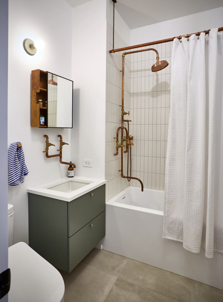 Bathroom with copper pipe shower, white curtain, green vanity, and wall-mounted mirror cabinet.