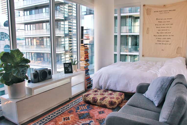 Bed with white linens and gray sofa in studio apartment