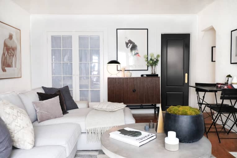 Living room with light gray sofa, black door, David Hockney print, and portrait of male body