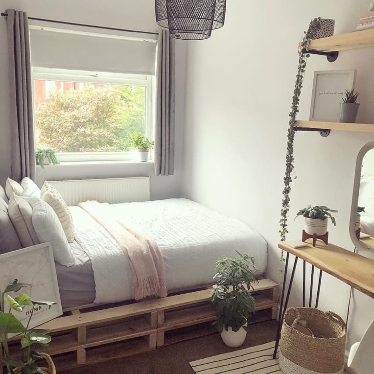pallet bed with gray, white, and pink bedding, surrounded by plants and wood decor