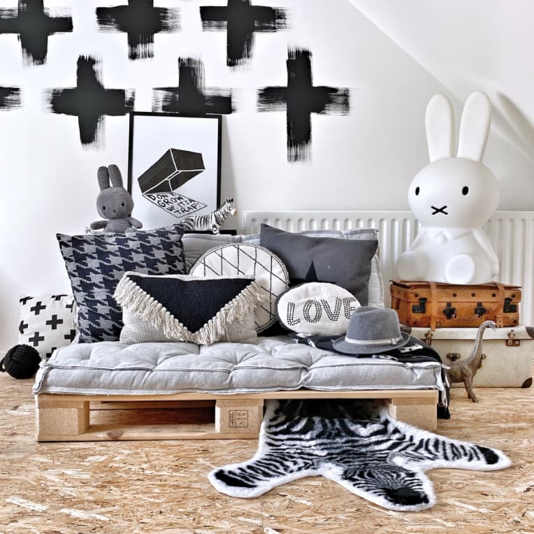 DIY daybed made with shipping pallets, against a white wall with black painted plus signs