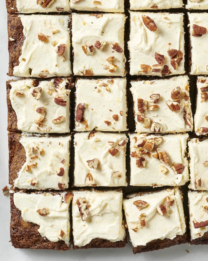 cut zucchini cake topped with cream cheese frosting and topped with chopped nuts on parchment paper on a marble surface