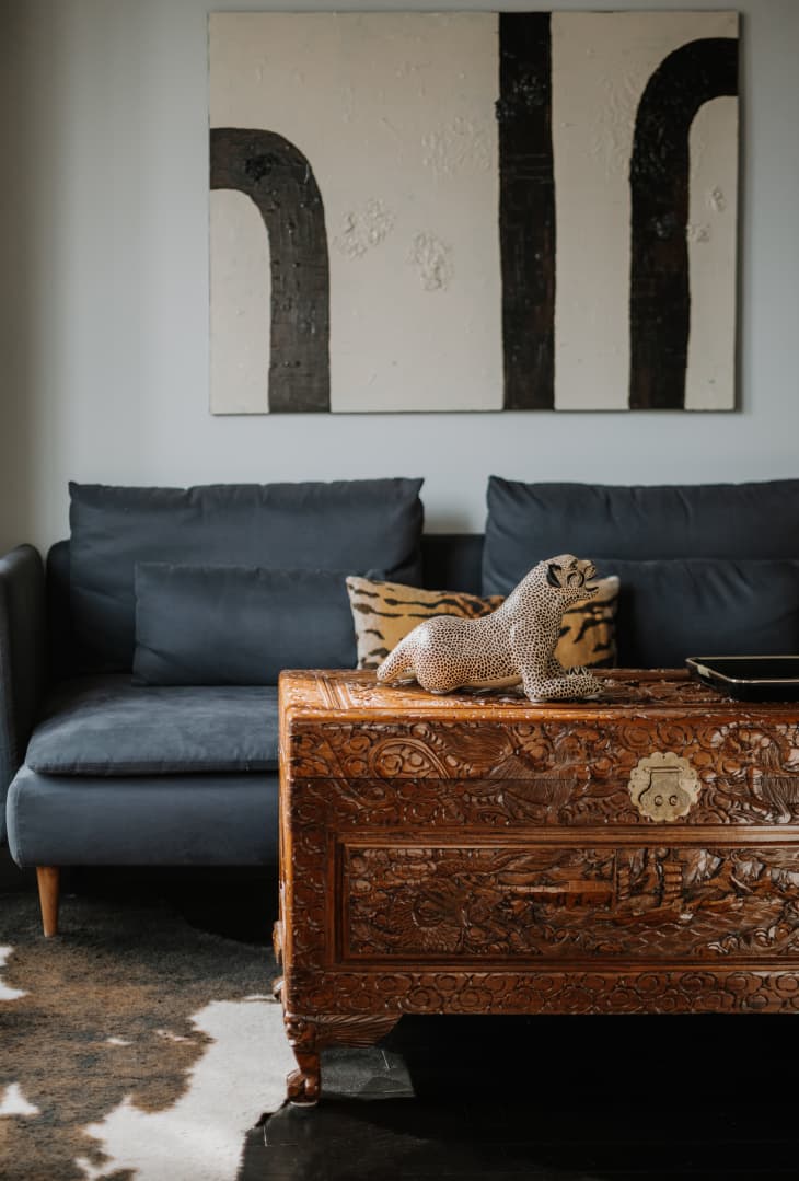A carved wood trunk in front on a modular blue sofa and a black and white painting on the wall.