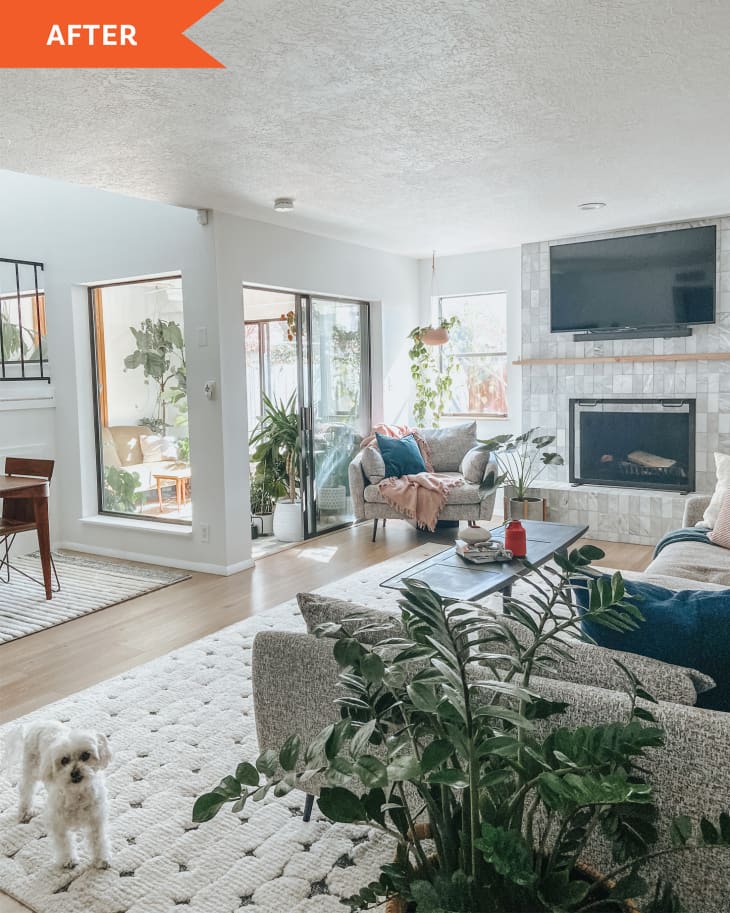 “After” photo of room that’s been completely redone and features a lot of DIY projects. Lot’s of white, tiled fireplace, white dog, gallery wall above sofa