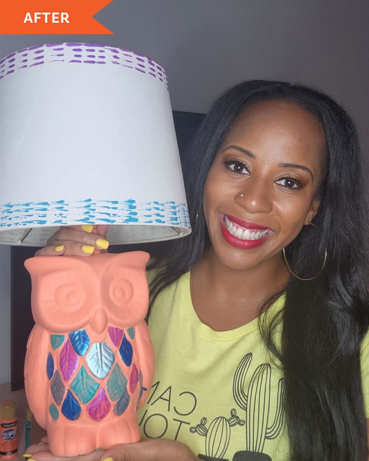 DIYer holding terra cotta owl lamp where the feathers have been painted in metallic blues and purples, and the shade has been painted with blue and purple patterns.