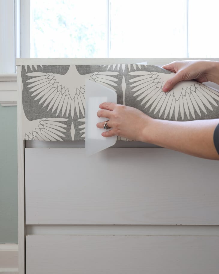 hands smoothing wallpaper onto a dresser