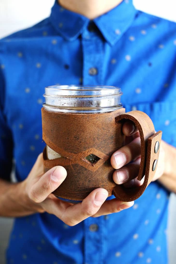 man holding a mason jar wrapped in a decorative leather sleeve
