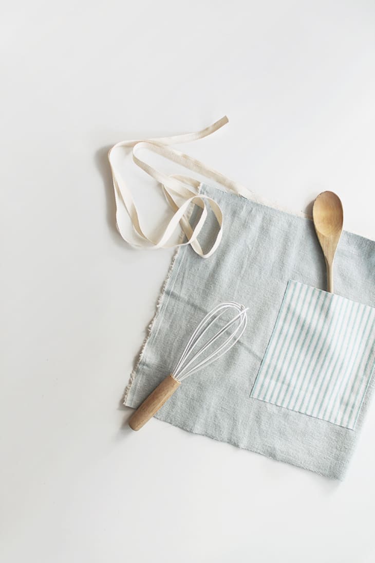Blue waist apron folded and shown with a wood spoon and a whisk
