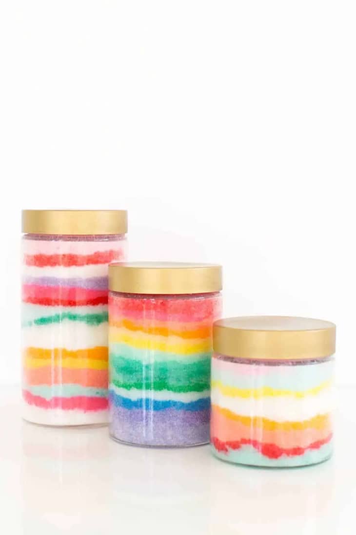 Three jars filled with colorful sugar scrub, filled to look like rainbow stripes from the side