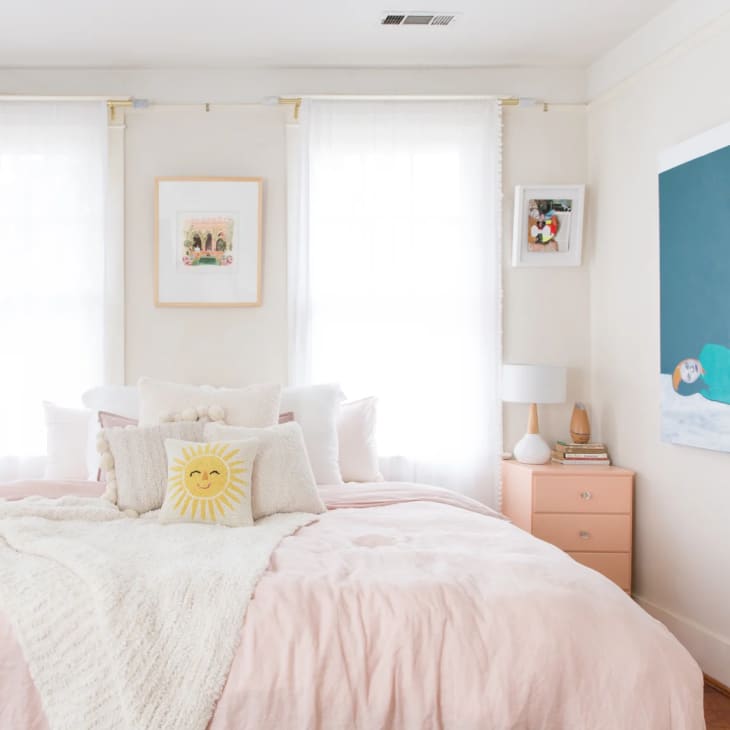 a light pink bedspread against two sunlit windows