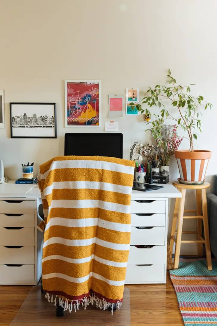 a beige-walled office space with a mustard yellow and white striped blanket draped over the desk chair