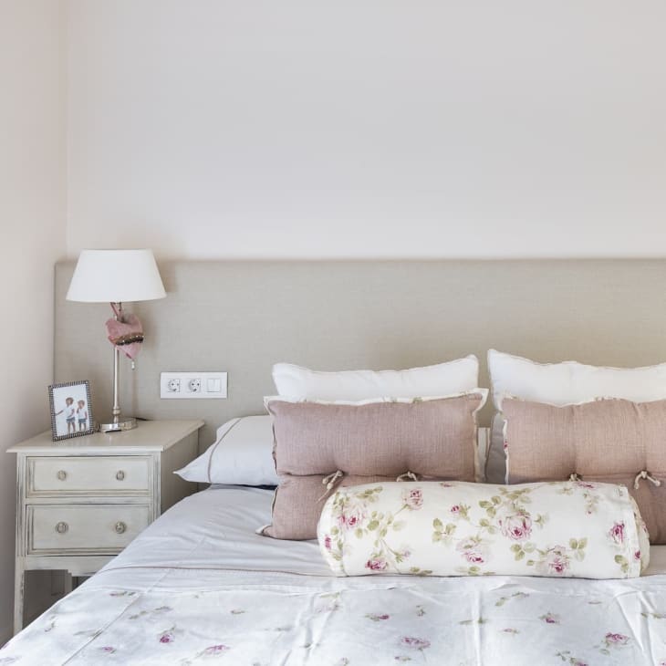 a beige headboard with a white bedspread and dusty rose throw pillows with floral accents