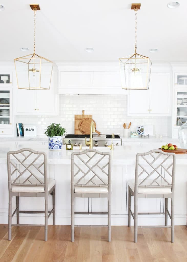 An all-white kitchen with a large island and three bar stools with a pattern on the back