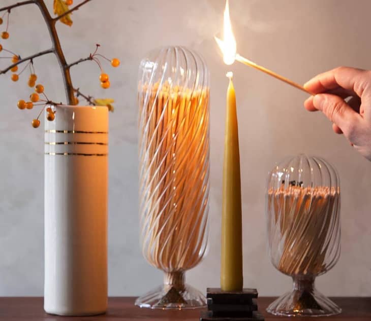 Someone lighting taper candle with Skeem design helix match. Matches are under cloche.