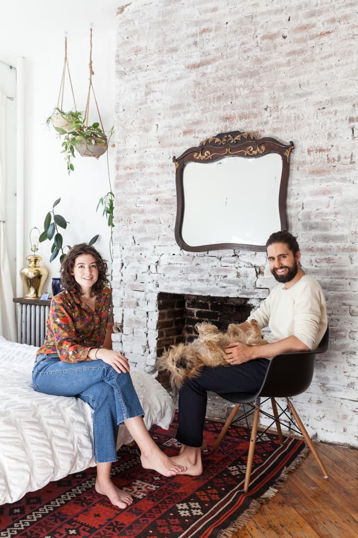 woman sitting on bed and man sitting in chair holding onto dog in cozy bedroom