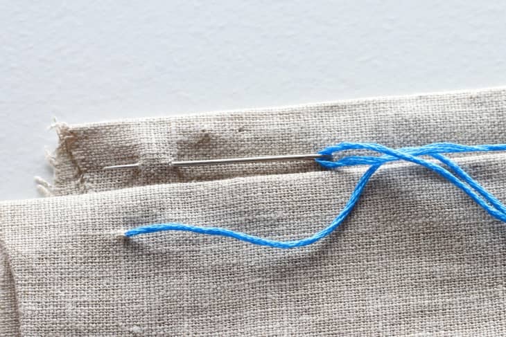 Needle piercing through top section of canvas material with blue thread