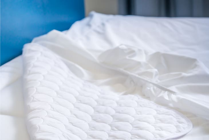 A white mattress cover is removed from a bed's corner