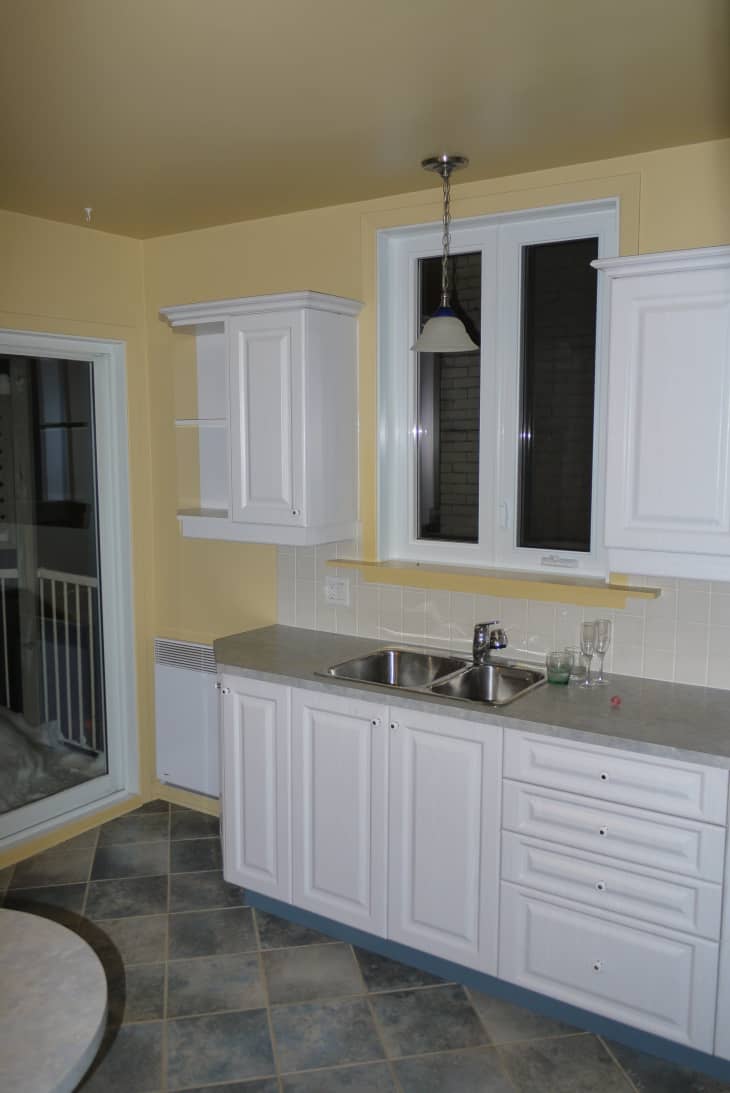 A dark kitchen with white cabinets and pale yellow walls