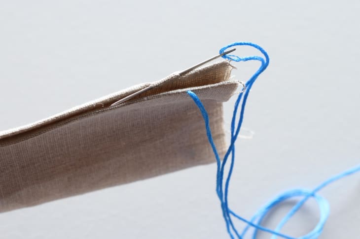 Needle going through edge of canvas-like material with blue thread