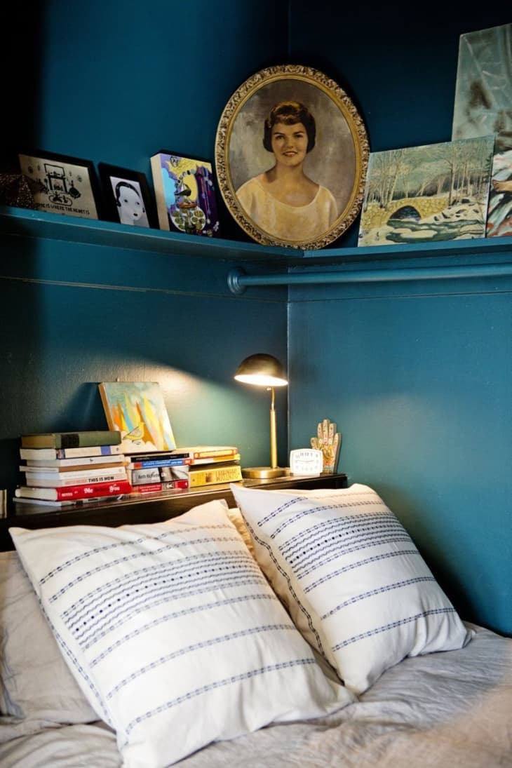 A closet converts into a bedroom painted with dark peacock blue and designed with picture frames, books, and memorabilia